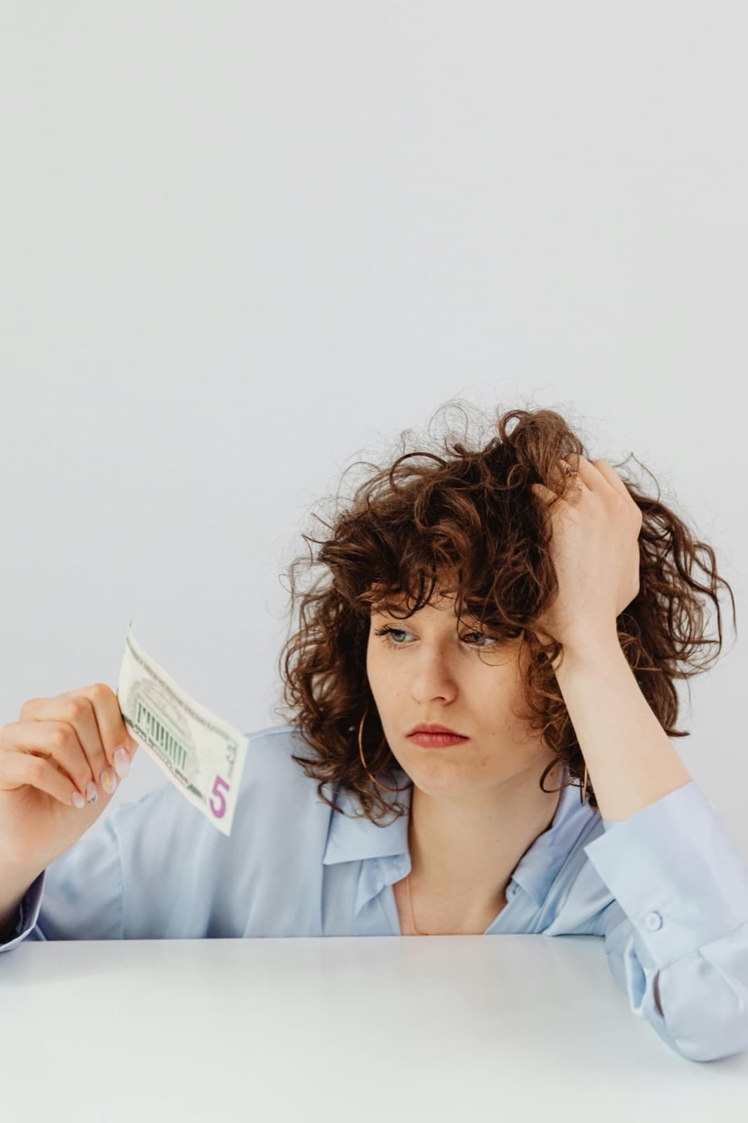 Small business owner holding a five dollar bill, looking worried about website pricing